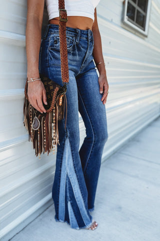 Person wearing blue flared jeans and a white crop top, holding a fringed brown handbag.