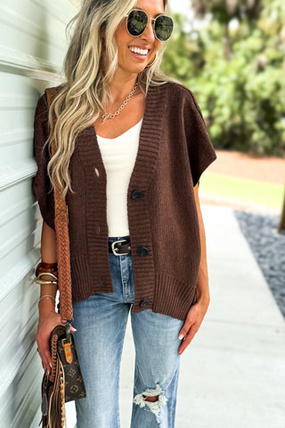 Woman wearing a brown cardigan with cream top and medium wash jeans 