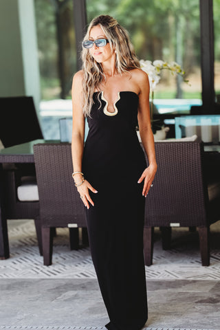 Woman in a black dress standing in an outdoor setting with chairs and tables.