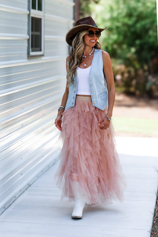 Woman wearing a pink tulle skirt, white top, and denim vest outdoors.