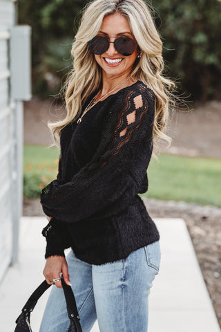 Woman wearing a black sweater with lace details and blue jeans outdoors.