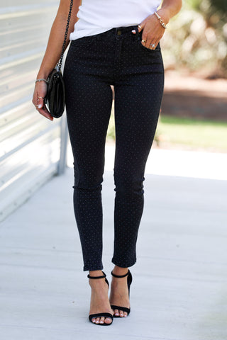Person wearing dark grey polka dot jeans with a white top and black sandals outdoors.