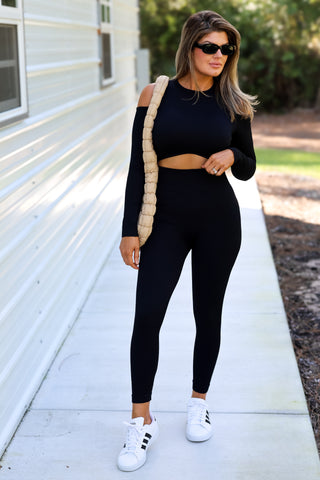 Woman in black athletic wear with white sneakers standing on a sidewalk.