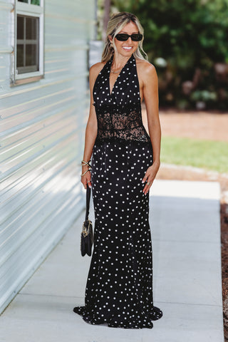 Woman wearing a black and white polka dot mermaid fit dress and gold bracelets carrying a black bag