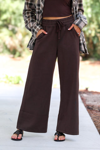 Woman standing outdoors wearing espresso brown cropped pants, and a matching espresso brown active top.
