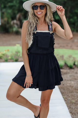 Woman wearing a black dress with ruffled layers and a wide-brimmed hat outdoors.
