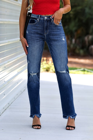 Person wearing blue jeans with a red top and black sandals on a white surface.