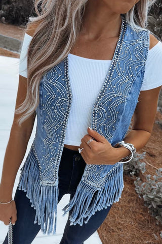 Woman wearing a denim beaded vest with fringe details outdoors.
