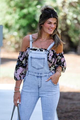 Woman wearing a floral blouse and denim overalls outdoors