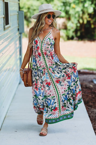 Woman wearing a floral dress carrying a straw bag and wearing a beige hat 