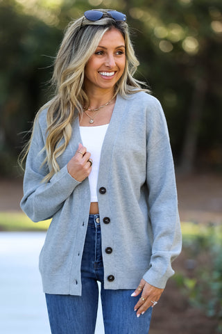Woman wearing a light grey cardigan with black buttons outdoors